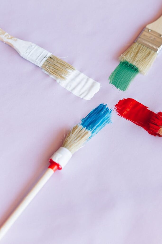 Four paintbrushes with vibrant colors on a light surface.